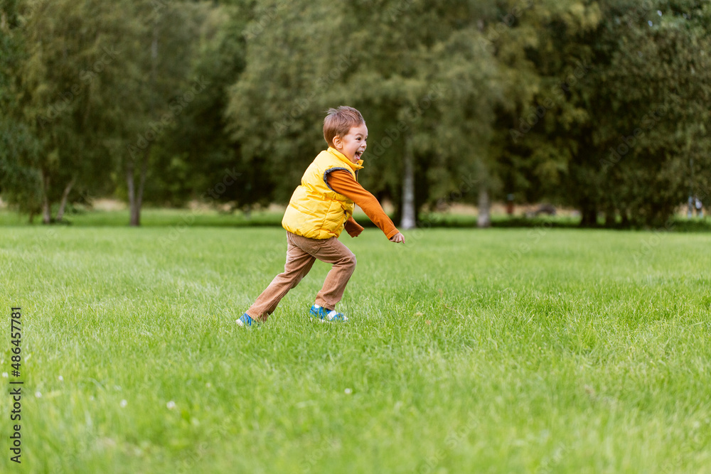 childhood, leisure and people concept - happy little boy running on green field at park