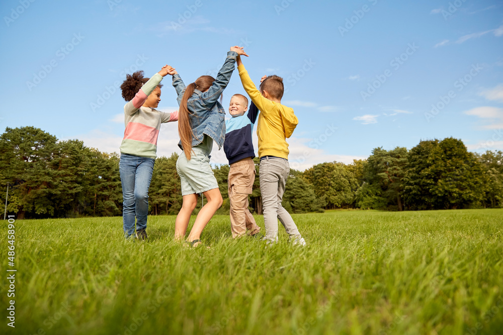 childhood, leisure and people concept - group of happy kids playing round dance at park childhood, leisure and people concept - group of happy kids playing round dance at park