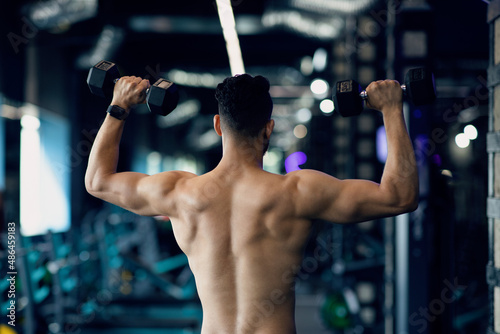 Bodybuilding Concept. Rear View Of Muscular Man Training With Dumbbells In Gym