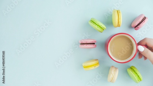 Top view of multicolored French Macarons cookies and a cup of coffee on a pastel blue background
