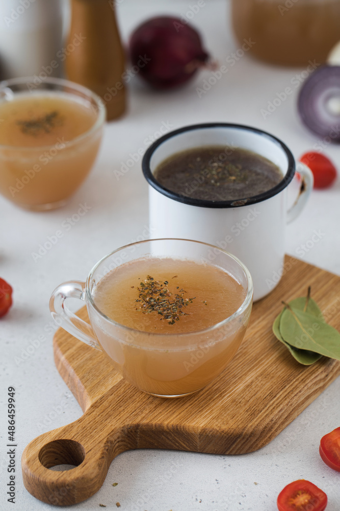 Homemade bone broth in mugs with spices on a wooden stick with bay leaf. Homemade bone broth in mugs with spices on a wooden stick with bay leaf.
