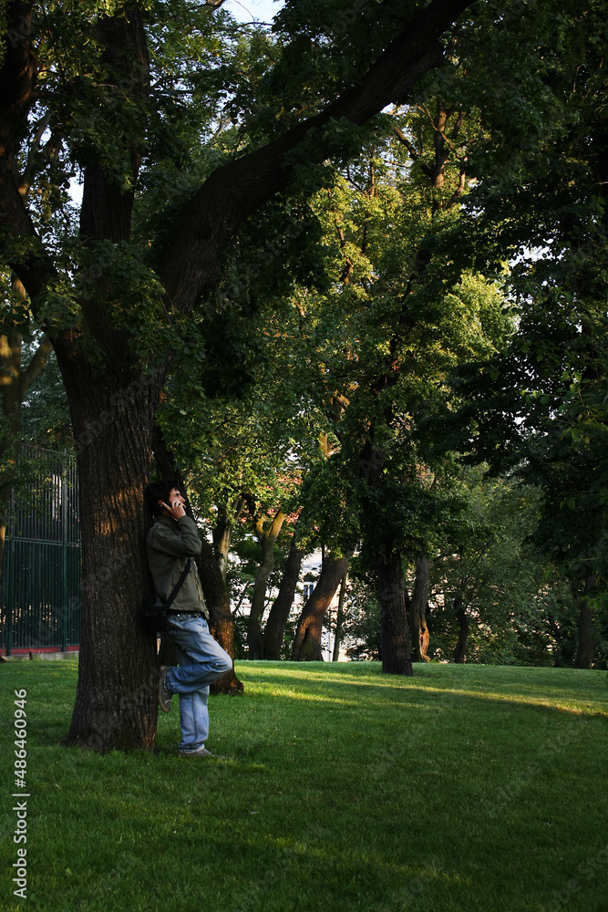 Fototapeta premium A man stands by a tree and talks on the phone