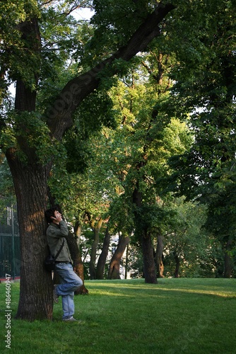 A man stands by a tree and talks on the phone