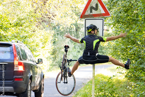 Fototapeta Naklejka Na Ścianę i Meble -  A falling cyclist bumps into a road sign next to road with traffic