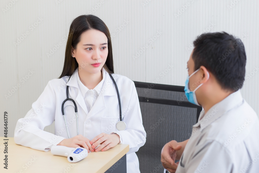 Asian professional woman doctor talking with a man patient about his symptom stomach ache while they put on a face mask to prevent Coronavirus disease and Thermometer on table In the hospital
