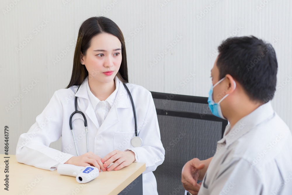 Asian professional woman doctor talking with a man patient about his symptom stomach ache while they put on a face mask to prevent Coronavirus disease and Thermometer on table In the hospital Asian professional woman doctor talking with a man patient about his symptom stomach ache while they put on a face mask to prevent Coronavirus disease and Thermometer on table In the hospital