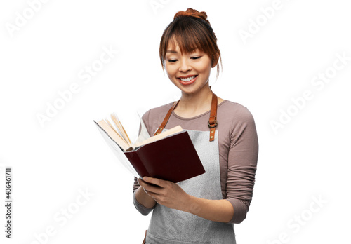 cooking, culinary and people concept - happy smiling woman in apron reading cook book over white background