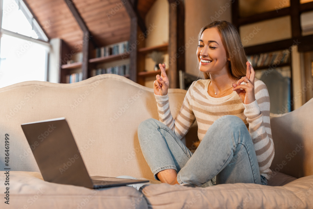 Hopeful woman crossing fingers making wish using pc Hopeful woman crossing fingers making wish using pc