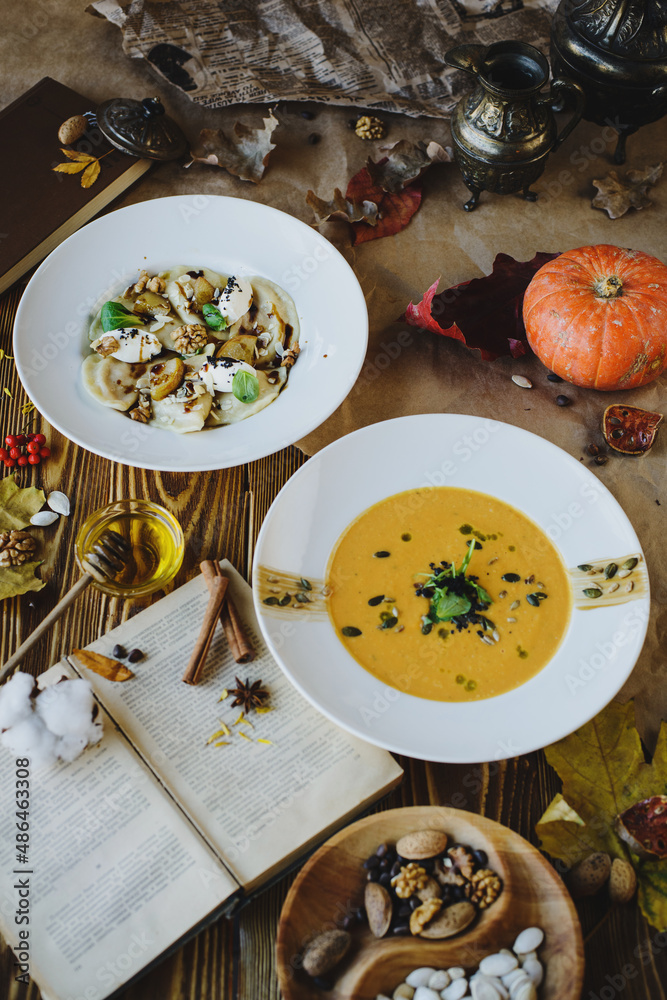 Autumn dishes: dumplings with walnuts, feta, honey and pear and pumpkin soup with seeds on a textured wooden table Autumn dishes: dumplings with walnuts, feta, honey and pear and pumpkin soup with seeds on a textured wooden table