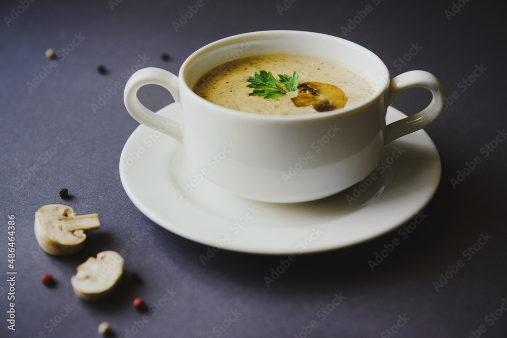 Mushroom cream soup in a white cup on a gray background. Next to mushrooms, peppers and a spoon Mushroom cream soup in a white cup on a gray background. Next to mushrooms, peppers and a spoon