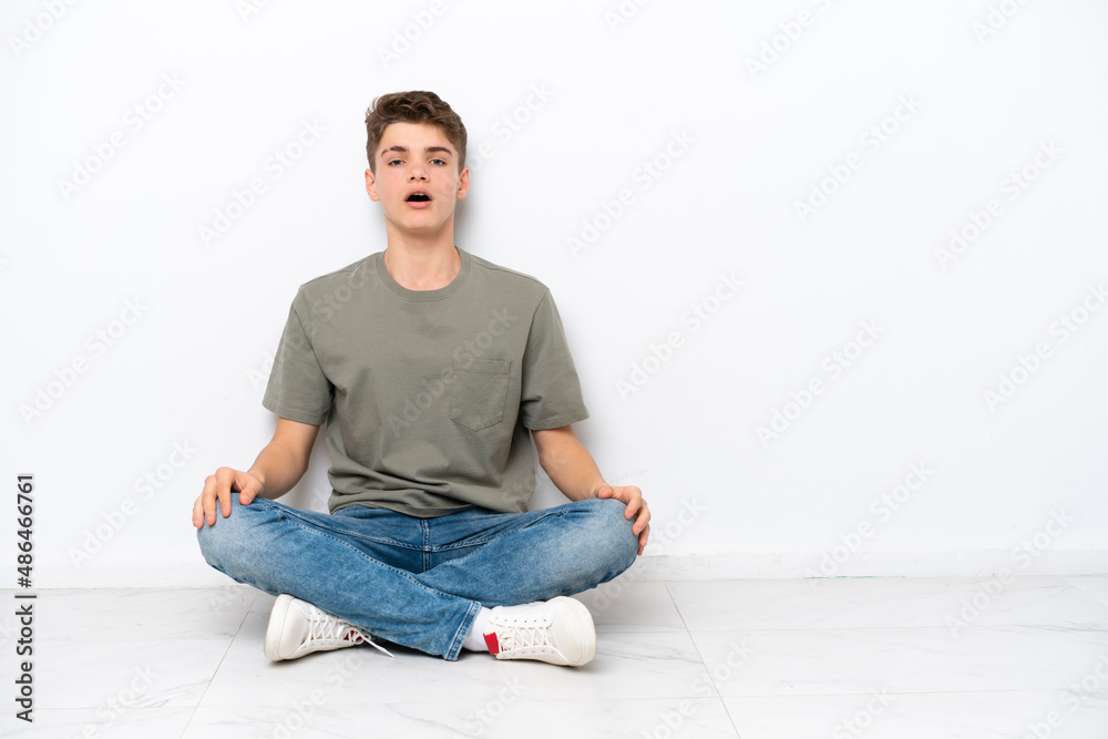 Teenager Russian man sitting on the floor isolated on white background with surprise facial expression Teenager Russian man sitting on the floor isolated on white background with surprise facial expression