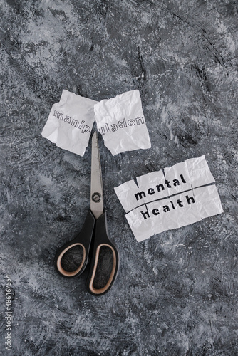 Manipulation text on crumpled piece of paper which is getting cut with scissors next to Mental Health text, psychology and emotional healing