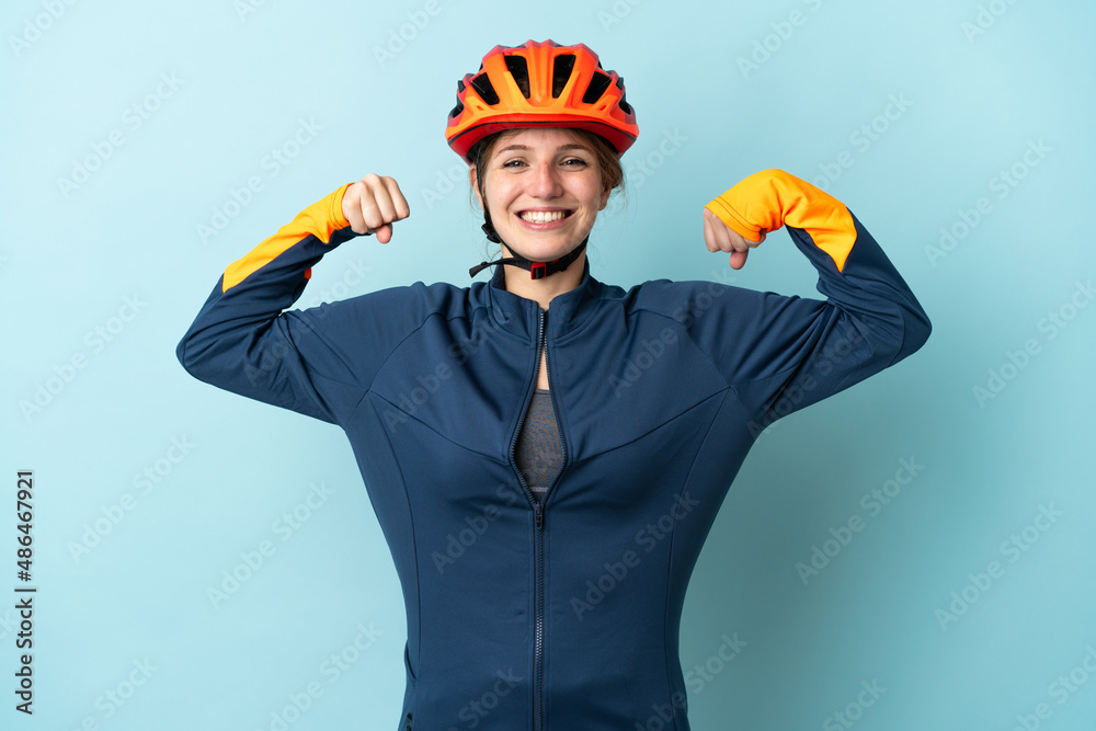 Young cyclist woman isolated on blue background doing strong gesture - obrazy, fototapety, plakaty 