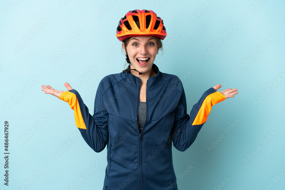 Young cyclist woman isolated on blue background with shocked facial expression - obrazy, fototapety, plakaty 
