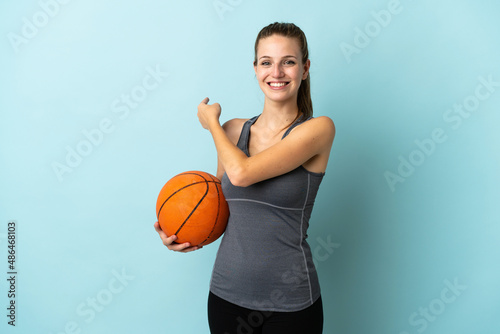 Young woman playing basketball isolated on blue background pointing back