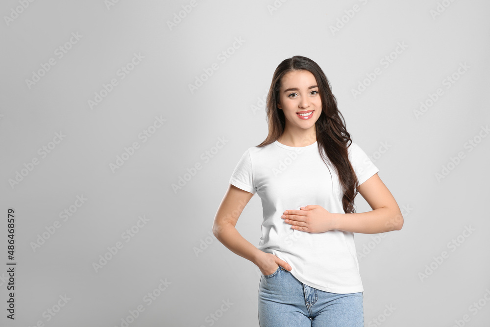 Happy healthy woman touching her belly on light grey background, space for text Happy healthy woman touching her belly on light grey background, space for text