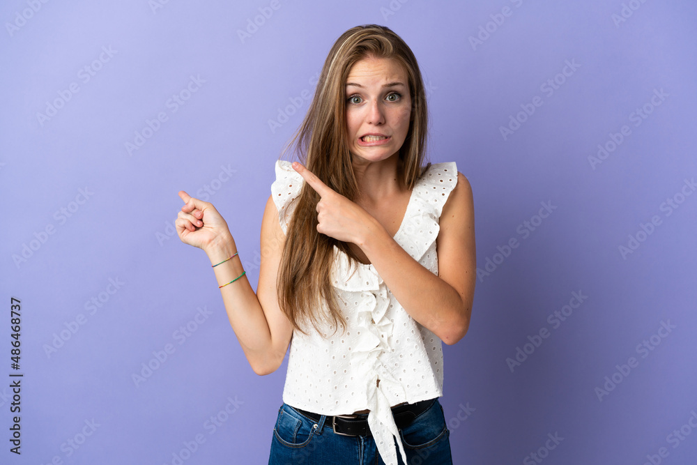 Young caucasian woman over isolated background frightened and pointing to the side Young caucasian woman over isolated background frightened and pointing to the side