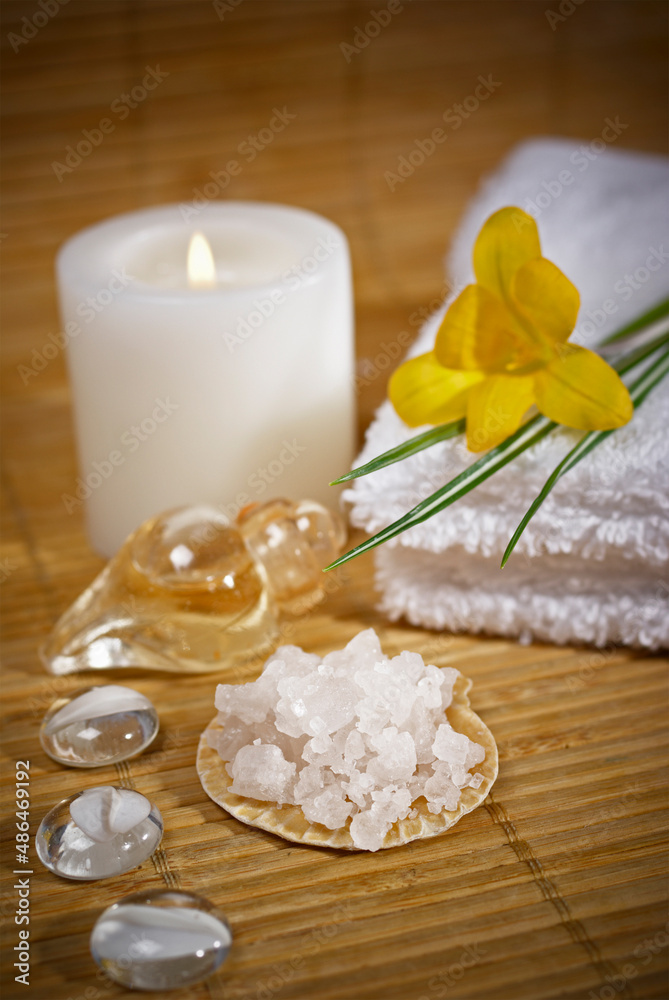 Spa composition on table in wellness center. Towels, flower, seashells, and bath salt on bamboo mat.