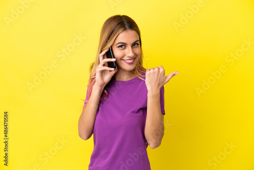 Young woman using mobile phone over isolated yellow background pointing to the side to present a product © luismolinero