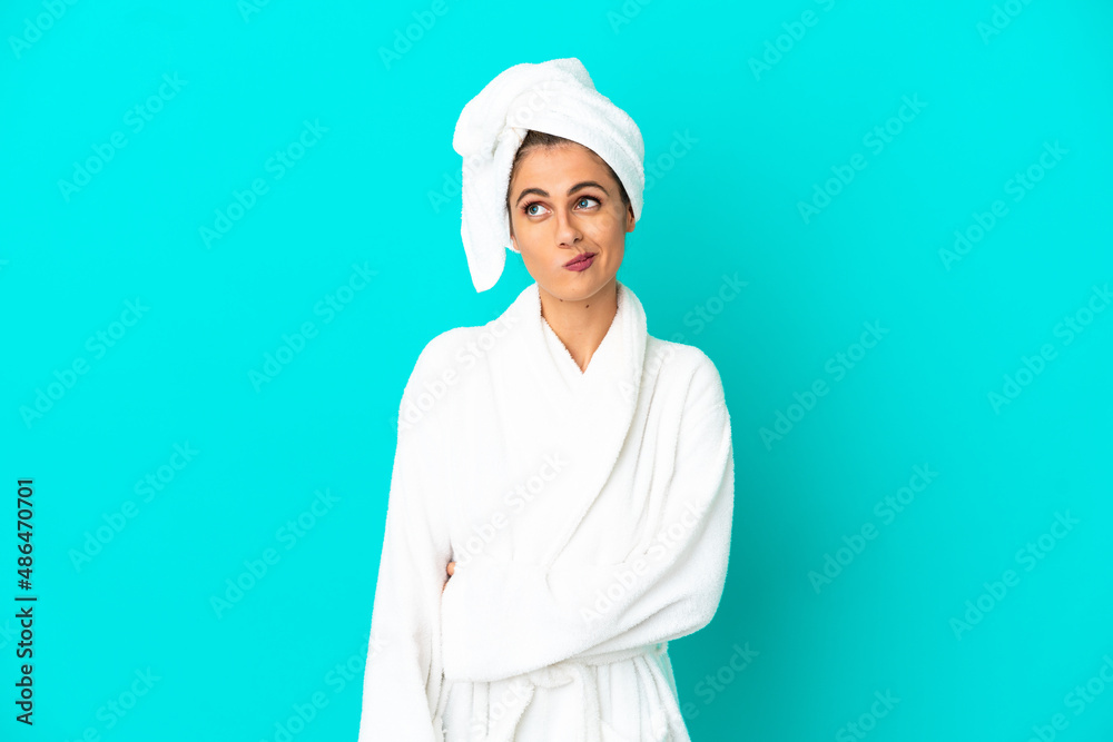 Young woman in a bathrobe over isolated blue background and looking up