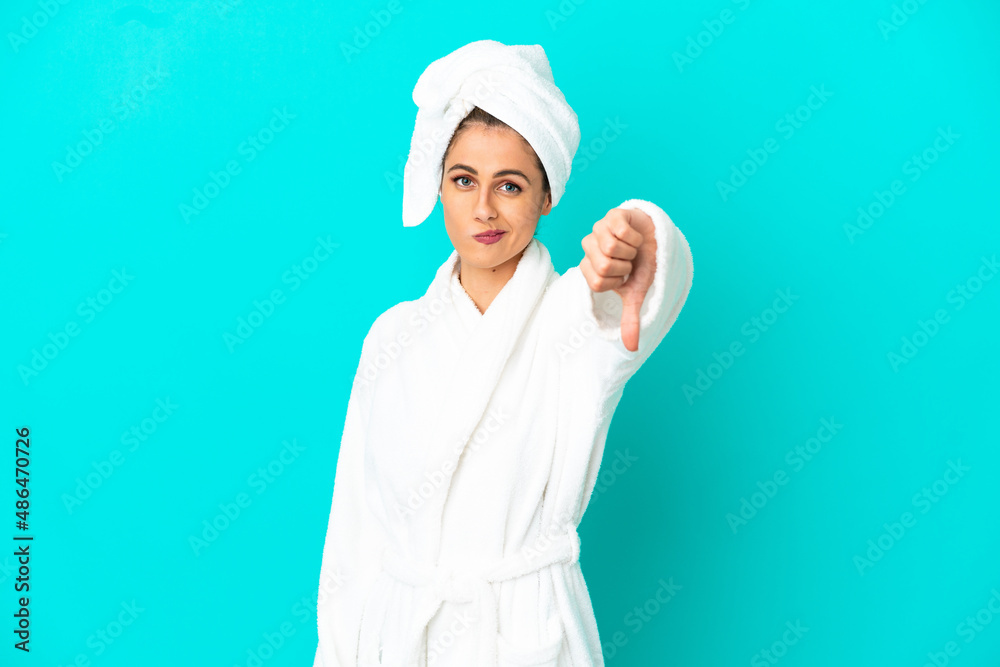 Young woman in a bathrobe over isolated blue background showing thumb down with negative expression