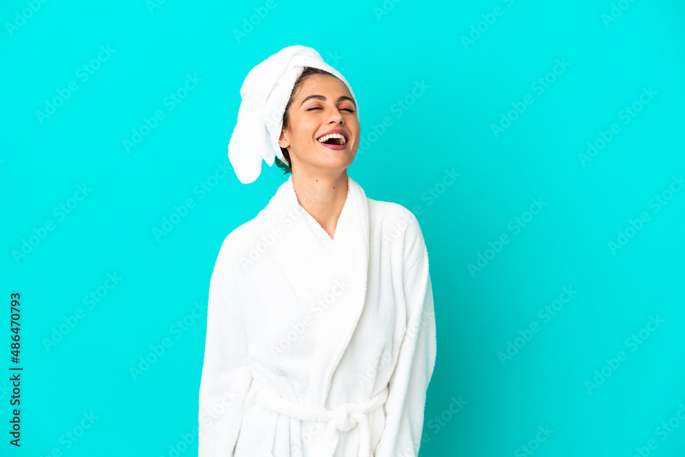 Young woman in a bathrobe over isolated blue background laughing Young woman in a bathrobe over isolated blue background laughing