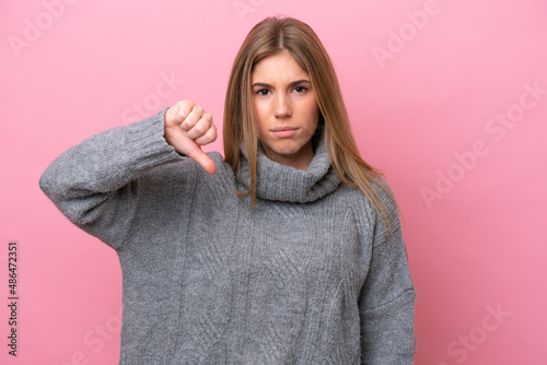 Young caucasian woman isolated on pink bakcground showing thumb down with negative expression © luismolinero