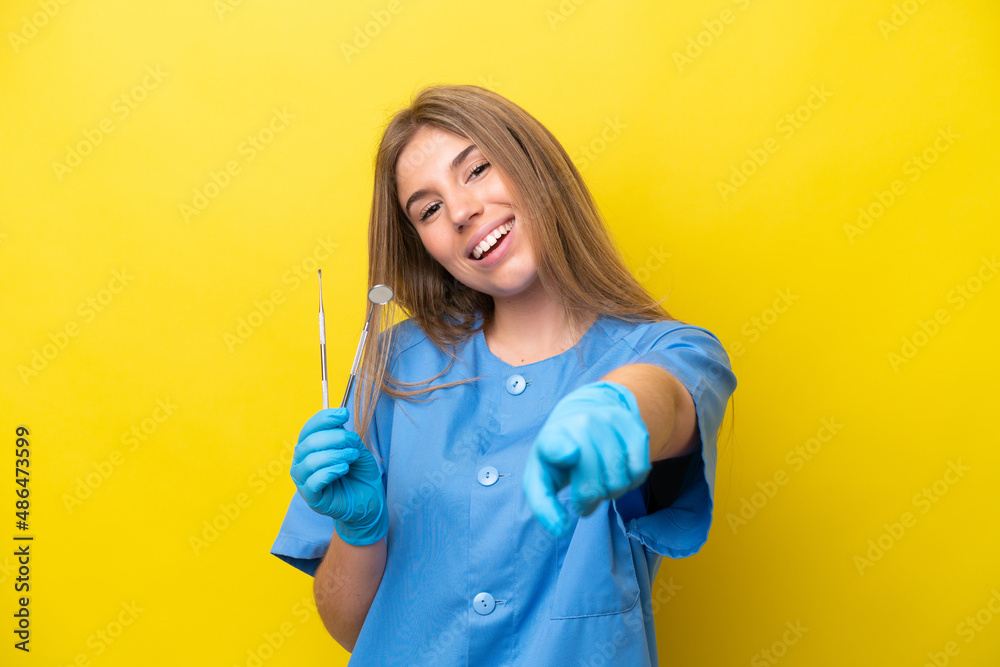 Dentist caucasian woman holding tools isolated on yellow background pointing front with happy expression Dentist caucasian woman holding tools isolated on yellow background pointing front with happy expression