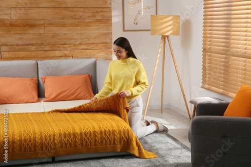 Young woman making bed in room. Modern interior with sleeper sofa