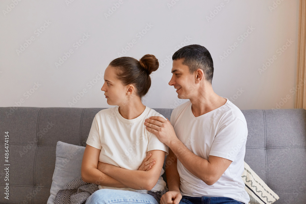 Indoor shot of young couple having conflict, angry offended woman sitting on couch and turning away from husband, having family fight or quarrel suffer from misunderstanding. Indoor shot of young couple having conflict, angry offended woman sitting on couch and turning away from husband, having family fight or quarrel suffer from misunderstanding.