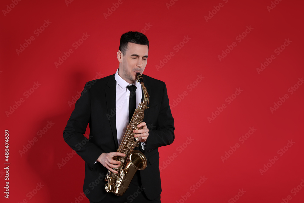 Fototapeta premium Young man in elegant suit playing saxophone on red background