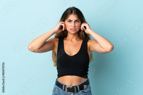 Young caucasian woman isolated on blue background frustrated and covering ears
