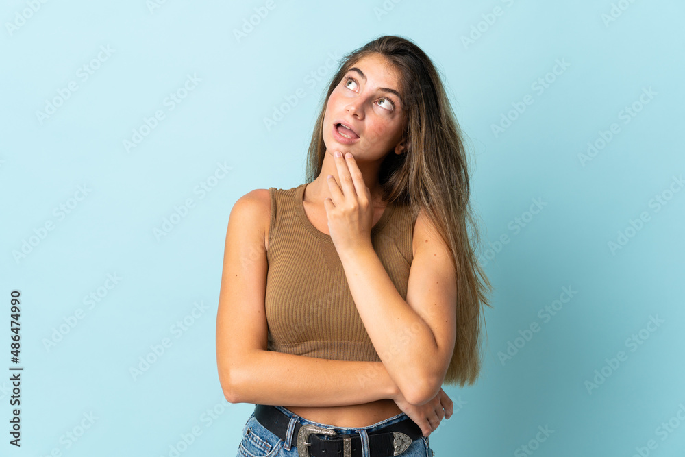Young caucasian woman isolated on blue background looking up while smiling Young caucasian woman isolated on blue background looking up while smiling