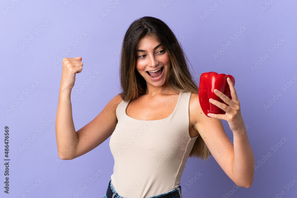 Young woman holding a pepper isolated on purple background celebrating a victory Young woman holding a pepper isolated on purple background celebrating a victory