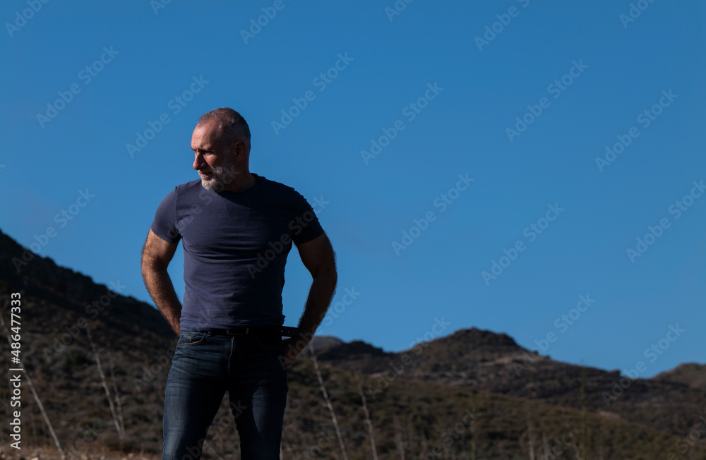 Adult man in jeans against sky and mountain on a sunny day