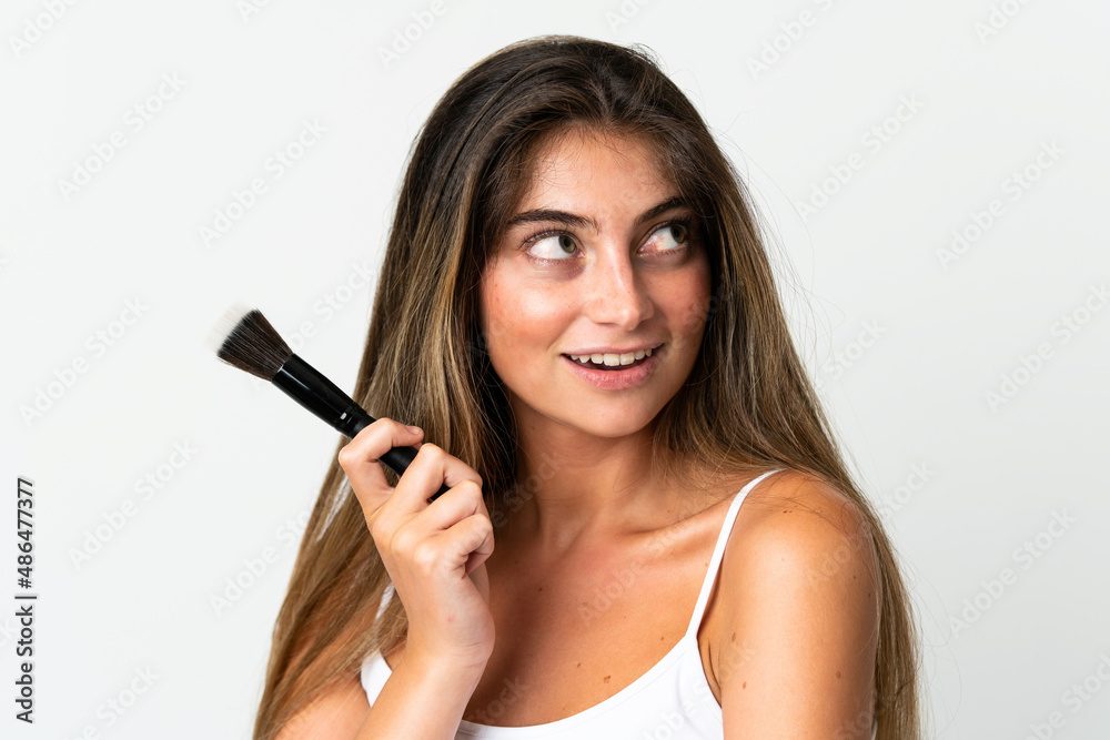 Young caucasian woman isolated on white background holding makeup brush and looking up Young caucasian woman isolated on white background holding makeup brush and looking up