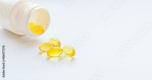White jar and yellow fish oil capsules on light background with copy space.