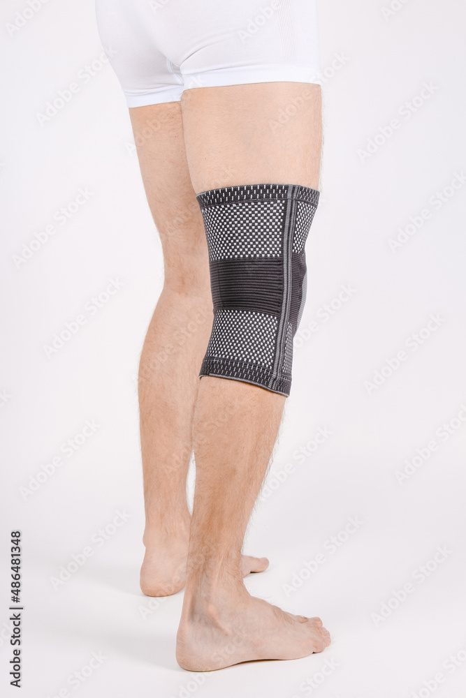 Knee Support Brace on leg isolated on white background. Elastic orthopedic orthosis. Anatomic braces for knee fixation, injuries and pain. Protective knee joint bandage sleeve. Trauma, rehabilitation Knee Support Brace on leg isolated on white background. Elastic orthopedic orthosis. Anatomic braces for knee fixation, injuries and pain. Protective knee joint bandage sleeve. Trauma, rehabilitation