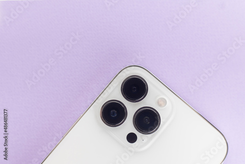 a white smartphone with three cameras lies on a purple background