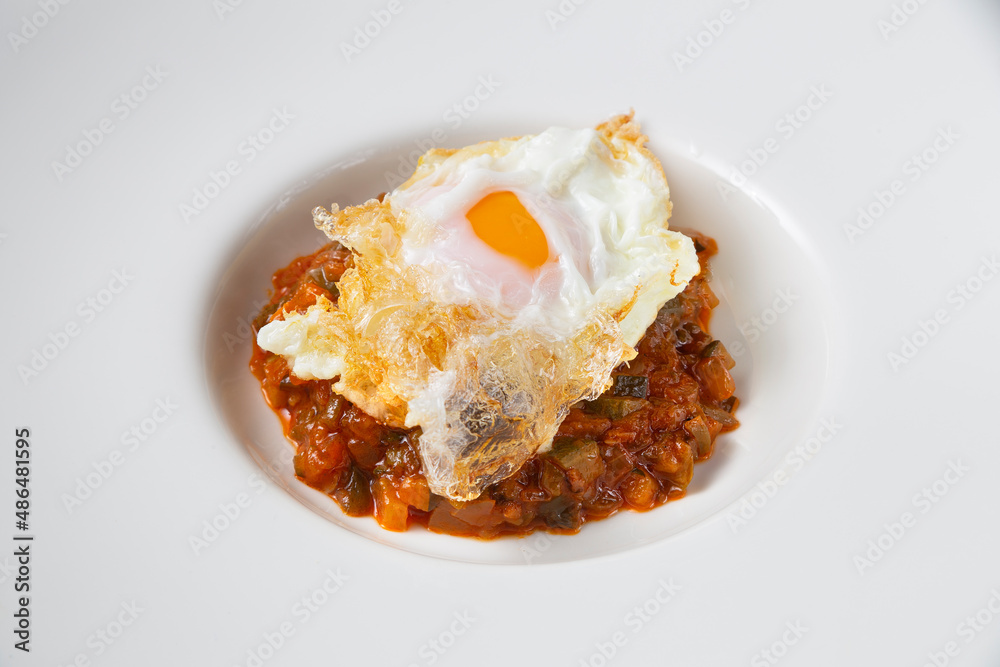 Close-up still life of ratatouille with fried egg on a white plate. Concept of traditional Spanish gastronomy. Close-up still life of ratatouille with fried egg on a white plate. Concept of traditional Spanish gastronomy.