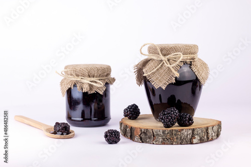 Sweet homemade blackberry jam in small glass jar with wooden spoon and fresh berries on a white isolated background. photo