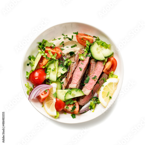 Fresh salad and creamy hummus are topped with veggies and perfectly grilled steak in this Mediterranean Steak Bowl. isolated on white background, top view 