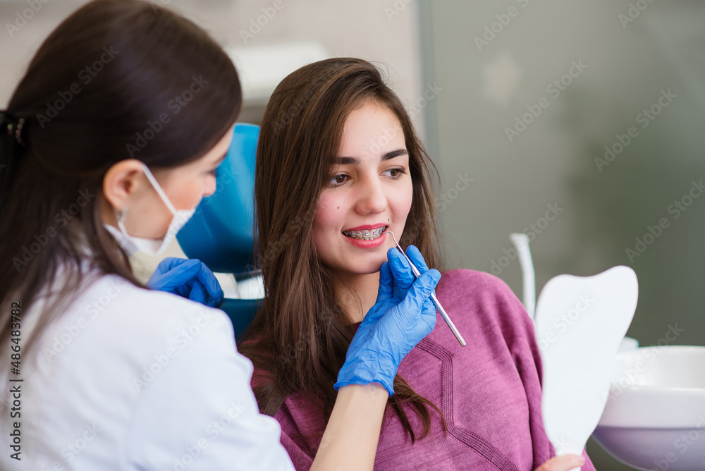 Obraz premium Close up of dentist hand using dental forceps while putting orthodontic braces on female patient teeth. Woman having dental procedure in clinic. Concept of dentistry and orthodontic treatment.