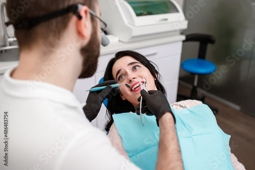 Dentist and his dental assistant examining a terrified young patient in dental clinic