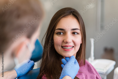 Close up of woman with brackets receiving dental braces treatment in clinic. Orthodontist using dental mirror and forceps while putting orthodontic braces on patient teeth. Concept of dentistry.
