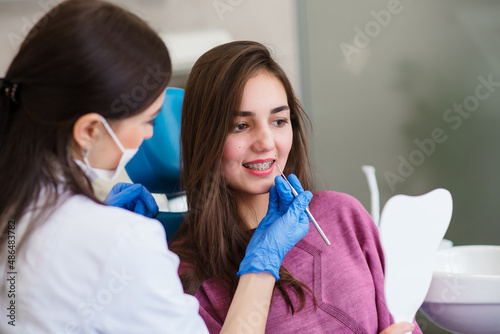 Close up of dentist hand using dental forceps while putting orthodontic braces on female patient teeth. Woman having dental procedure in clinic. Concept of dentistry and orthodontic treatment. photo