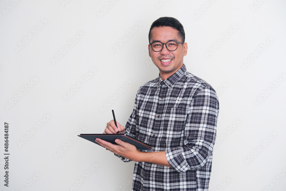 Adult Asian man smiling confident while working using his mobile tablet gadget