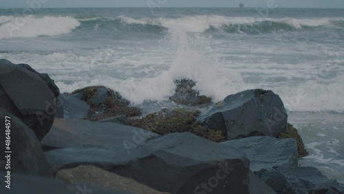 Small waves push in from the ocean against sharp, dark rocks covered in barnicles and limpits whilst the setting sun drools cool blue colours into the sky and ocean to give a small chill photo