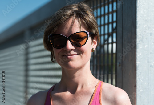 Muscled white woman with sunglasses posing against a metal fence with bare shoulders, Brussels, Belgium © Werner