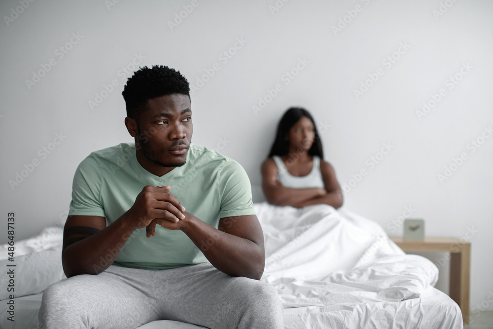 Obraz premium Depressed sad young black man ignores offended lady after quarrel sits on bed in bedroom interior, copy space